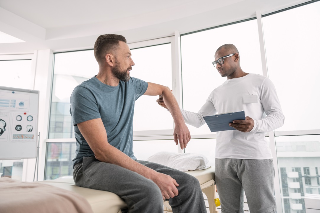 A man sitting on the edge of his bed talking to another man.