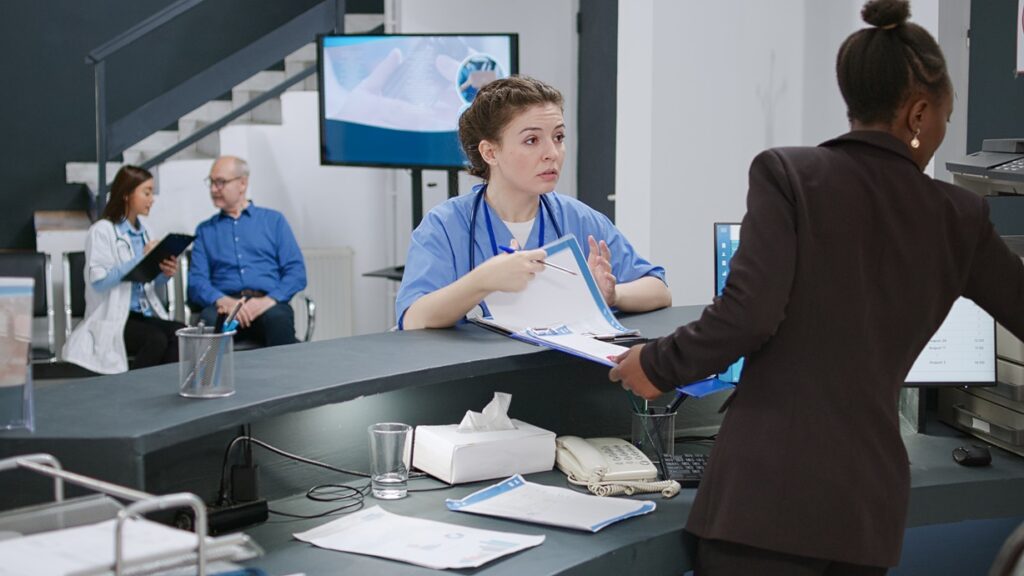 Nurse assisting patient at reception desk.