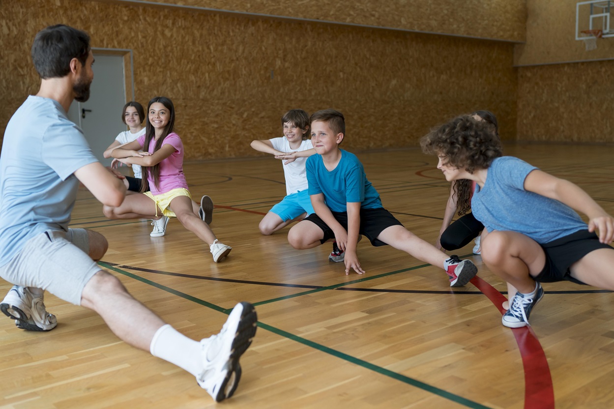 Kids stretching with their coach in gym.